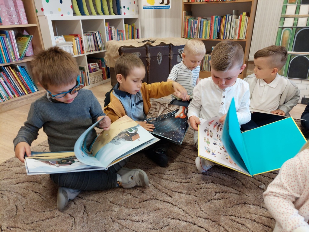 dzieci siedzące na dywanie z zainteresowaniem oglądające duże ksiązki